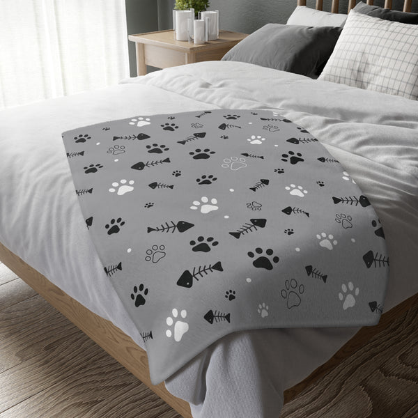 Reversible pet print polyester blanket in black and white, featuring paw prints and fish bones, displayed on a cozy bed.