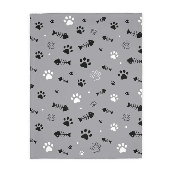 A folded pet lover's blanket with paw prints and fish bones, highlighting the plush texture and the two-sided reversible design.