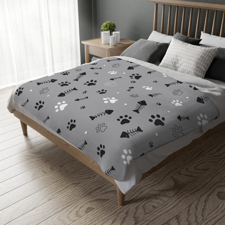 Close-up of a reversible pet blanket on a cozy bed showcasing the detailed paw print and fish bone design on both sides, with a focus on the neat stitched edges.