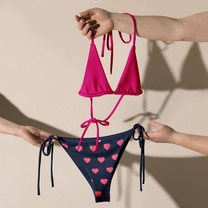 Holding a recycled polyester bikini set in magenta and heart print, combining eco-friendly materials with fashionable design.